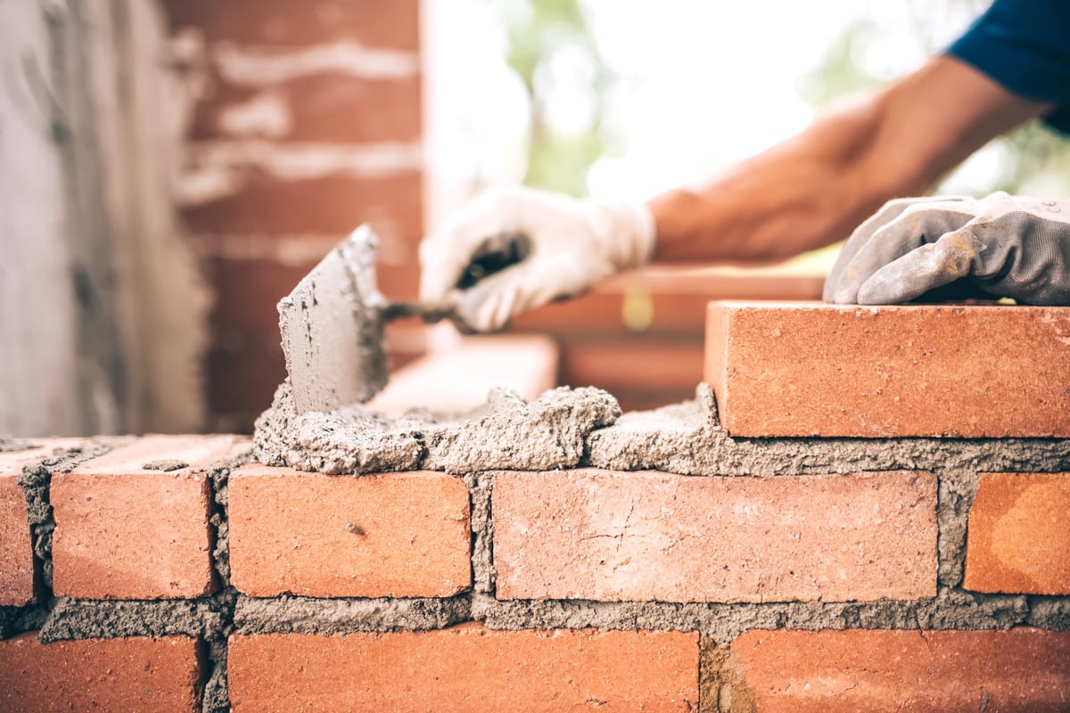 Bricklayer installing brick masonry on exterior wall with trowel